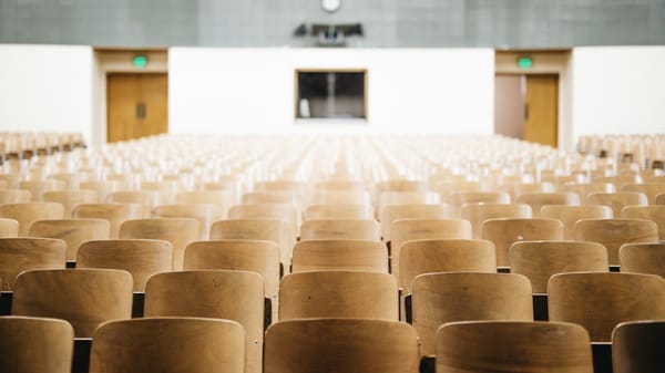 Rows of empty chairs with wooden backs in a college lecture hall. 